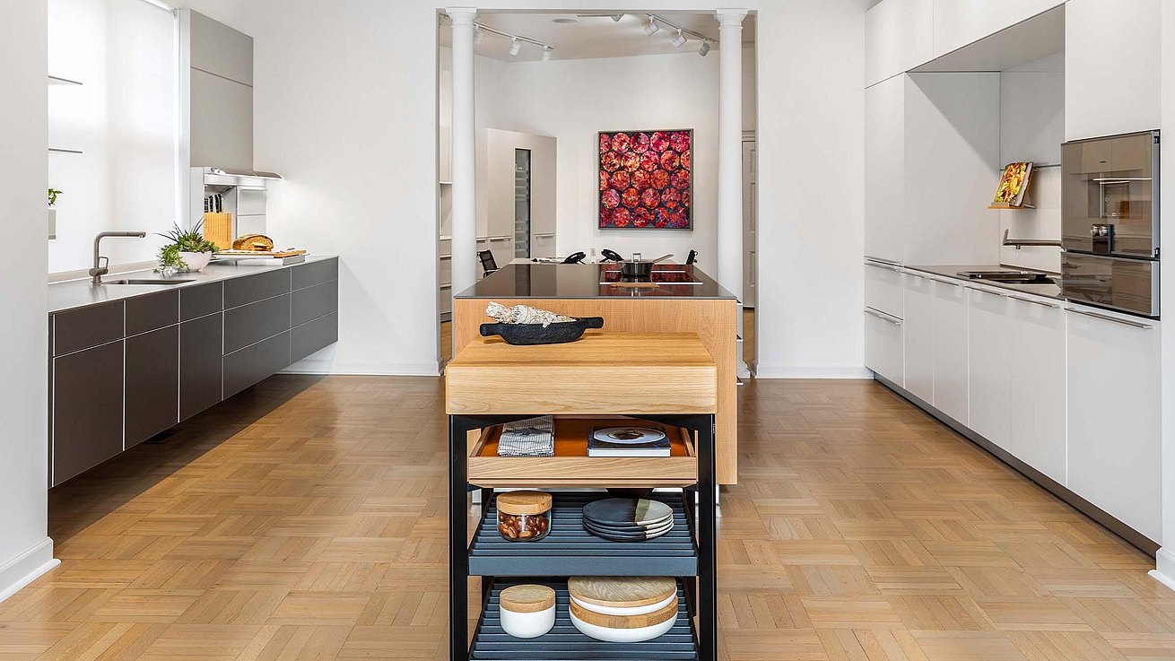 A photo that catches the symmetrical lines of the showroom with bulthaup b3 wall hanging base units on the left / dark aluminum finish, stainless steel countertop and function boxes in one end. On the right there is a bulthaup b3 / white matte lacquer finish and light grey quarts countertop. The island has the same light grey quarts countertop and structured natural oak fronts finish. On close plan we have a bulthaup b solitaire with solid oak top.